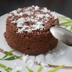 Un délicieux bowl cake au chocolat, saupoudré de sucre glace, prêt à être dégusté avec une cuillère.