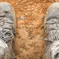 Mud-caked boots stand in wet earth, the bottom of shoes sticky from a muddy adventure.