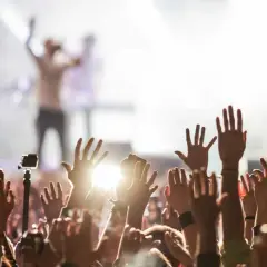 Tłum ludzi z podniesionymi rękami na koncercie, w tle artysta na scenie.