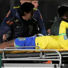 Neymar leży na noszach, z bólu trzymając się za twarz. Jego **neymar kontuzja** wygląda poważnie, a sztab medyczny otacza go troską.
