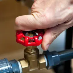 Dłoń obraca czerwony zawór grzybkowy, który jest częścią instalacji wodnej.