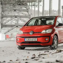 Röd VW Up med vinterdäck står på snöig mark under en bro. Ett vw up problem kan vara att den fastnar i snön.