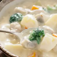 A spoonful of creamy Japanese white stew, filled with tender chicken, potatoes, broccoli, and carrots, ready to be savored.