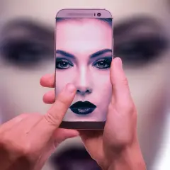 Dłonie trzymają smartfon, na ekranie którego widać twarz kobiety z mocnym makijażem. To przykład zaawansowanej fotografia obliczeniowa.