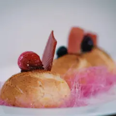 Un ou une profiterole décoré d'une framboise, d'une tuile de chocolat et de barbe à papa rose.