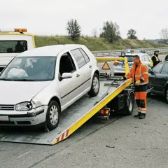 Srebrny samochód na lawecie, obok stoi pomoc drogowa i policja.