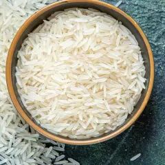 Chicchi di riso basmati in una ciotola e sparsi su una superficie scura. Le proprietà del riso basmati lo rendono un alimento leggero e digeribile.