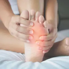 Mani che massaggiano la pianta del piede, evidenziando un'area arrossata che simboleggia il dolore.