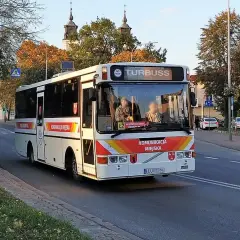 Biały autobus miejski z napisem "KOMUNIKACJA MIEJSKA" i "TURBUSS" jedzie ulicą. To część codziennych, busy przewozy po polsce.