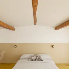 Chambre mansardée avec poutres apparentes. Quel mur peindre pour un effet cosy ? Le mur derrière le lit, avec sa tête de lit beige, semble idéal.