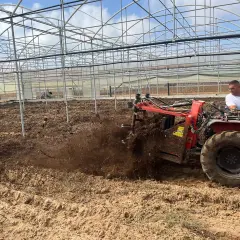 Trattore aratura in serra, lavorando il terreno per arricchirlo di sostanza organica.