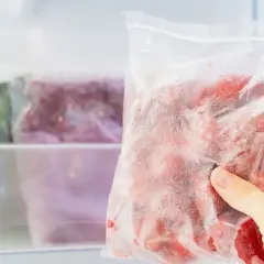 Ręka wyjmuje z zamrażarki worek z mrożonymi owocami. Czy jogurt można mrozić? Tak, ale najlepiej w małych porcjach.