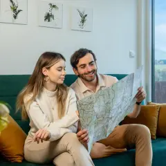 Para planuje podróż, przeglądając mapę. W tle widać krajobraz z domkami, przypominający widok z **Osolina**.