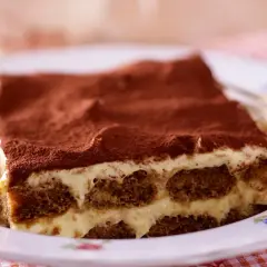 Ein Stück Tiramisu, ein Klassiker der italienischen Nachspeisen, auf einem Teller mit Kakaopulver bestäubt.