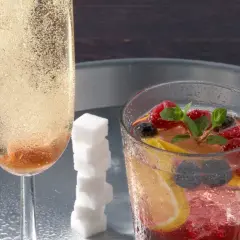 Ein prickelnder Champagner-Cocktail mit Beeren und Zitrone, daneben ein Glas mit sprudelndem Champagner und Zuckerspiralen.