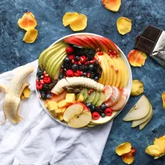 Plato de frutas variadas, incluyendo plátano, manzana, kiwi, bayas y cítricos. Es bueno comer fruta por la noche.