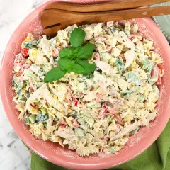 En krämig pastasallad med kyckling, grönsaker och majs, perfekt som pastasallad till grillat. Serveras i en rosa skål med trägafflar.