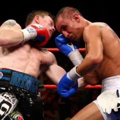 Two boxers exchange powerful boxing punches in the ring. One fighter lands a blow to the head, while the other attempts to counter.