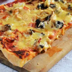 Pyszna pizza capriciosa z pieczarkami i szynką, roztopionym serem, na drewnianej desce.