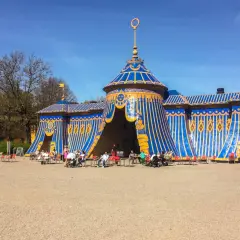 Blå och gul tältliknande byggnad med folk som sitter vid bord utanför i haga parken.