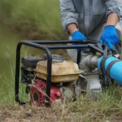 Maintenant, comment démonter une pompe à eau de jardin : une personne en gants bleus manipule le tuyau d'une pompe à eau.