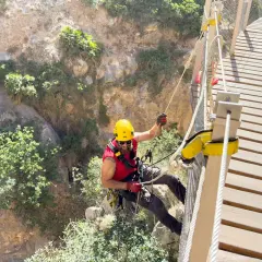 Man i gul hjälm klättrar på en hängbro längs Caminito del Rey, en dramatisk klippstig.
