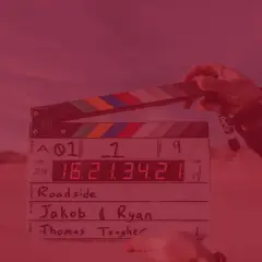 Dłoń trzyma klaps filmowy z zapisanymi informacjami o produkcji.