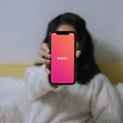 Osoba trzyma telefon z aplikacją Tinder. Chcesz wiedzieć, jak znaleźć kogoś na Tinderze?