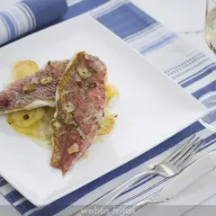 Dos deliciosos salmonetes al horno, con láminas de ajo y perejil, servidos sobre patatas. Un plato perfecto para disfrutar.