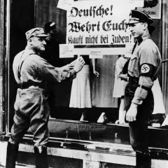 Ein SA-Mann klebt ein Plakat "Deutsche! Wehrt Euch! Kauft nicht bei Juden!" an ein Schaufenster. Dies ist ein Beispiel für den **Alltag im Nationalsozialismus**.