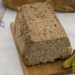 Domowy pasztet drobiowo-wieprzowy z wątróbką, podany z ogórkiem kiszonym na desce drewnianej.