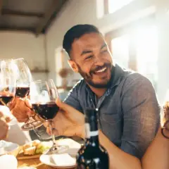 Des amis trinquent avec des verres de vin rouge lors d'une soirée dégustation vin conviviale, riant sous le soleil.