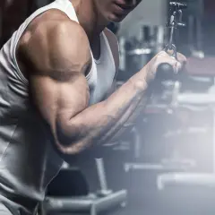 Mężczyzna ćwiczy mięsień trójgłowy na wyciągu. Widoczny jest jego umięśniony biceps i przedramię.