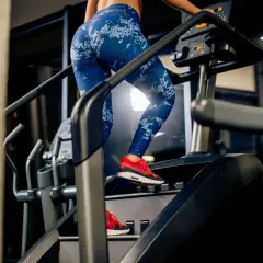 Femme en legging bleu sur un stepper, travaillant ses abdos fessiers. Entraînement intense pour sculpter son corps.