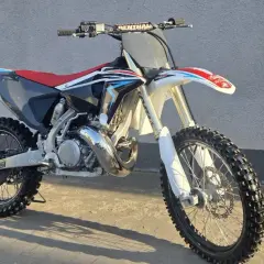 Motocykl crossowy Husqvarna CR 250 z czerwonym siedzeniem i czarnymi elementami, gotowy do jazdy po torze.