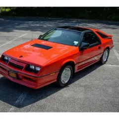 Pomarańczowy Dodge Daytona z czarnym dachem i spojlerem na parkingu.