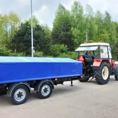 Czerwony traktor z niebieską plandeką na przyczepie. Zastanawiasz się, prawo jazdy kat T od ilu lat?