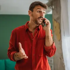 Mężczyzna w czerwonej koszuli rozmawia przez telefon, gestykulując.