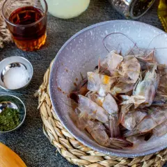 Cáscaras de camarón en un tazón, listas para hacer una sabrosa salsa americana. Ingredientes como tomate triturado, sal y hierbas acompañan.