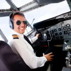 Uśmiechnięty pilot w okularach przeciwsłonecznych i słuchawkach w kokpicie samolotu. Zastanawiasz się, ile zarabia pilot samolotu?