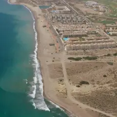 Vista aérea de la playa del Retamar, con el mar turquesa, arena dorada, urbanizaciones y un campo de golf.