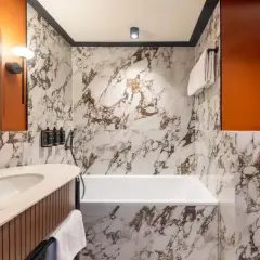 Elegancka łazienka w hotelu Mercure Gdynia z marmurowymi płytkami, wanną i umywalką.