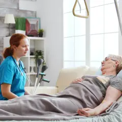Pielęgniarka rozmawia z pacjentką leżącą w łóżku. W tle widać kule, co sugeruje, że pacjentka może potrzebować wsparcia w odżywianiu dojelitowym.