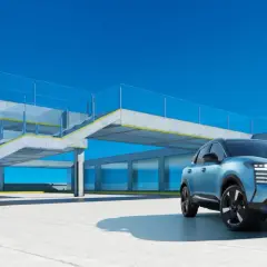 Niebieski Nissan Kicks stoi na betonowym placu przed nowoczesnym budynkiem z przeszklonymi oknami i betonowymi schodami.