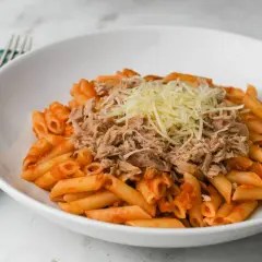 Macarrones con tomate y atún desmenuzado, cubiertos con queso rallado, servidos en un plato blanco.