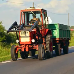 Czerwony traktor z przyczepą jedzie drogą. Zastanawiasz się, ile kosztuje przegląd ciągnika rolniczego?