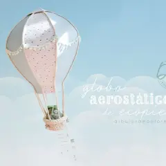 Un globo aerostático de manualidades con un peluche en la cesta, flotando en un cielo azul con nubes.
