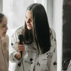 Kobieta z mikrofonem instruuje dziewczynkę, zwracając uwagę na ton głosu.