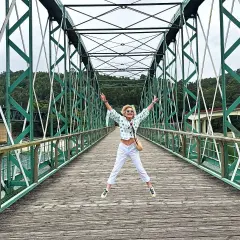 Mujer salta de alegría en un puente verde, disfrutando de las vistas. ¡Un lugar genial que ver en O Vicedo!