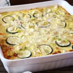 Pyszna zapiekanka z cukinii i mięsa mielonego, posypana parmezanem, w białym naczyniu żaroodpornym.